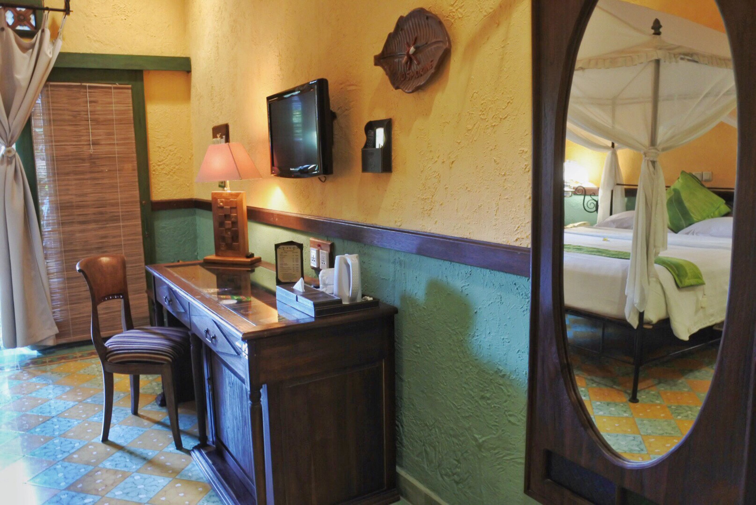 A room with a bed, a desk with a lamp, a television, and a mirror.