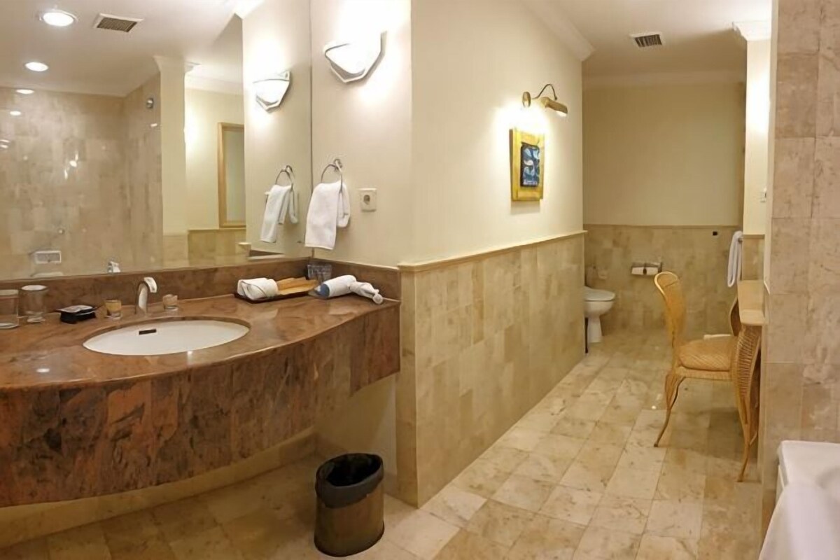 A bathroom with a marble sink, a mirror, a toilet, and a wicker chair.