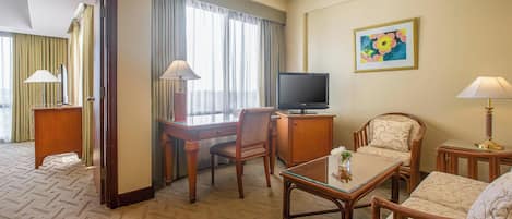 A hotel room with a wooden desk, a television, a sofa, and a painting on the wall.