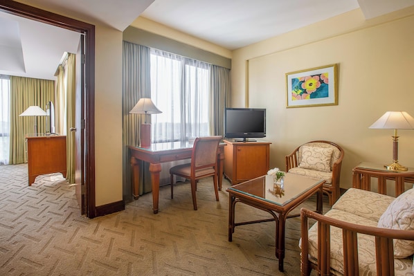 A hotel room with a wooden desk, a television, a sofa, and a painting on the wall. - Aryaduta Lippo Village (Curug)