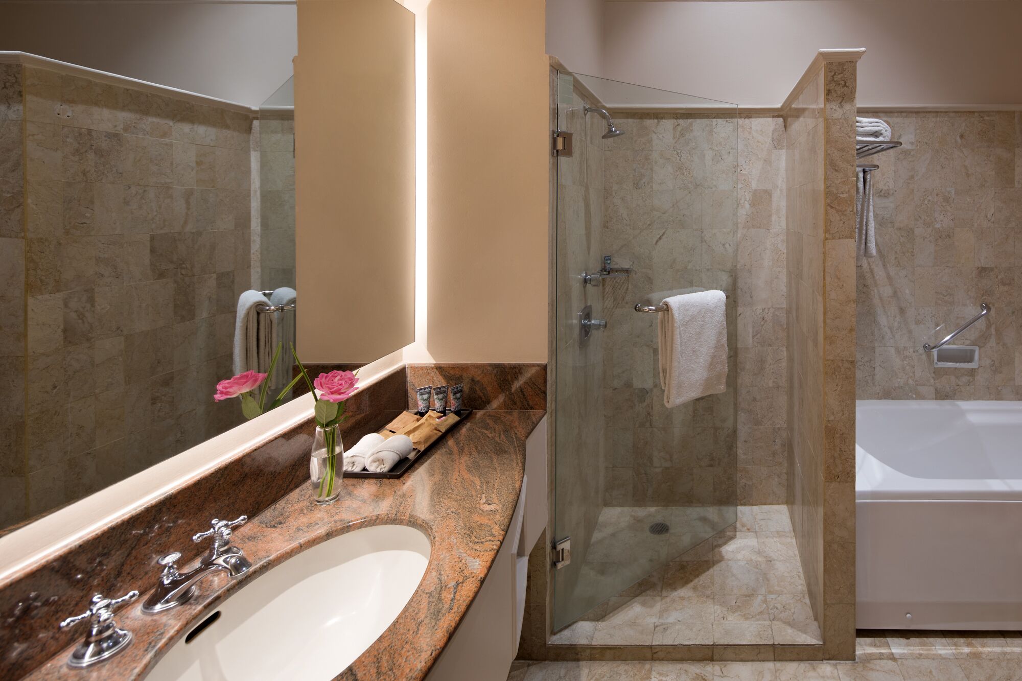 A modern bathroom with a glass-enclosed shower, a white bathtub, and a marble countertop with a sink and vanity.