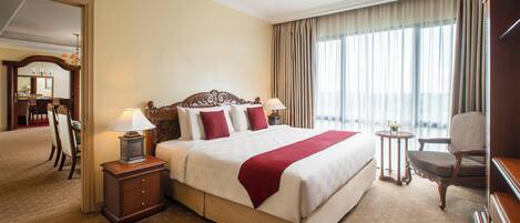 A hotel room with a large bed, a desk, a chair, and a small table with a lamp.