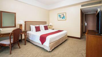 A hotel room with a bed, a desk, a chair, a television, and a painting on the wall.