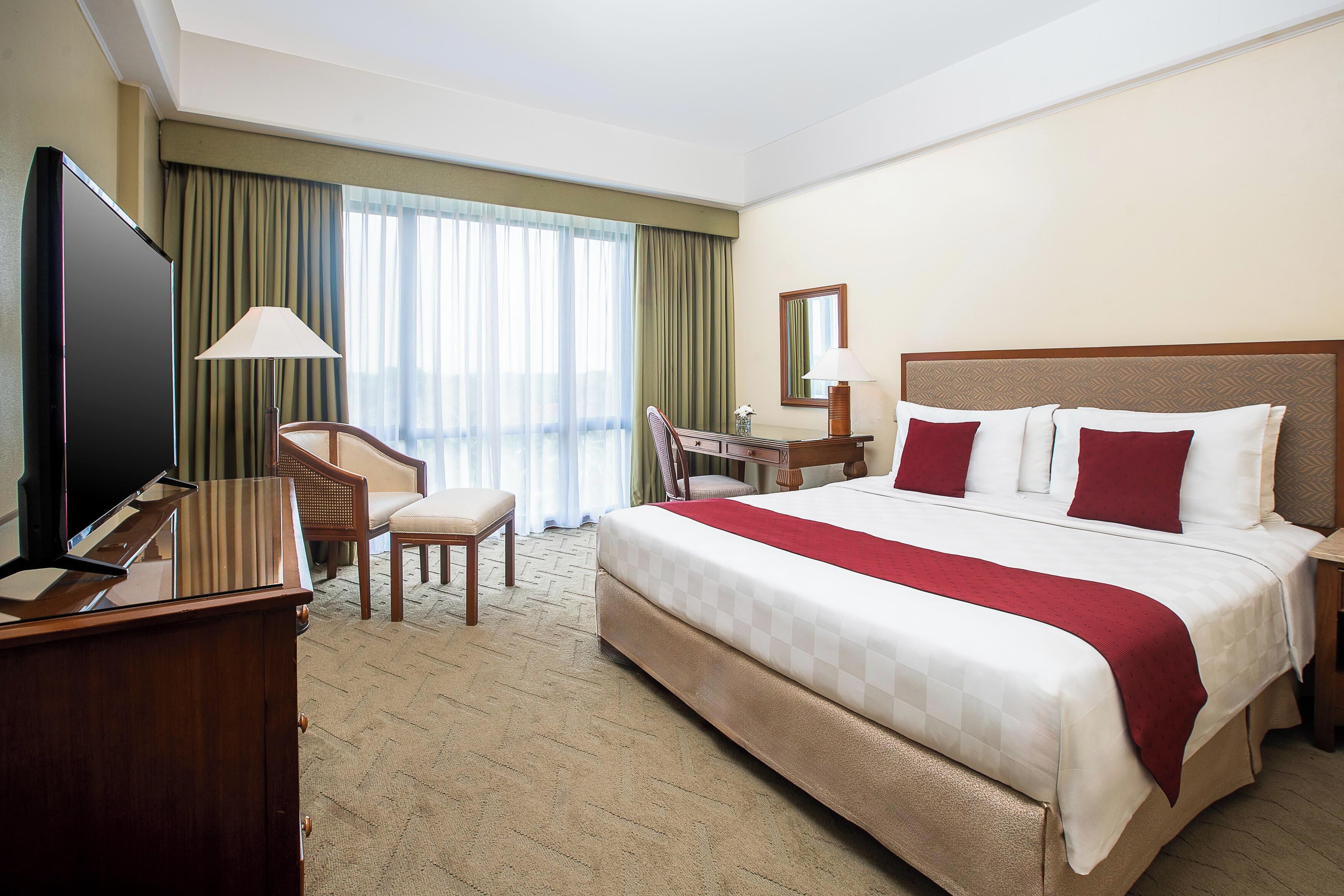 A hotel room with a large bed, a desk, a chair, a television, and a window with curtains.