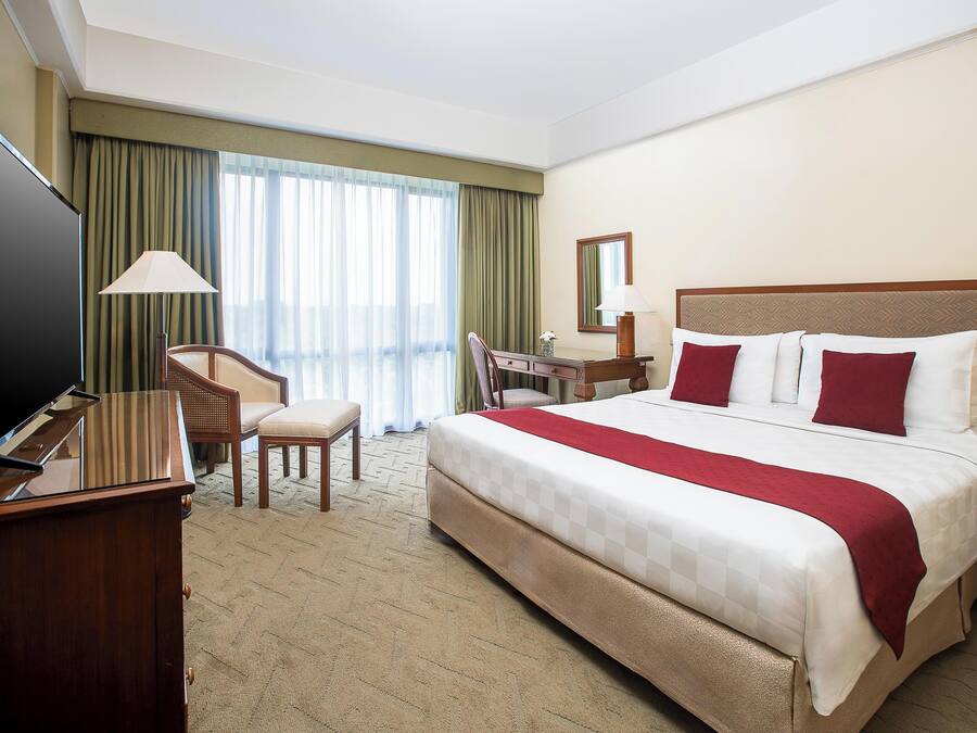 Habitación de hotel con una cama grande, un escritorio, una silla, un televisor y una ventana con cortinas.