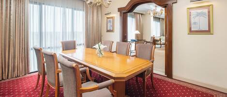 Un salón de conferencias con una mesa de madera, seis sillas, una araña y una alfombra roja con estampado.