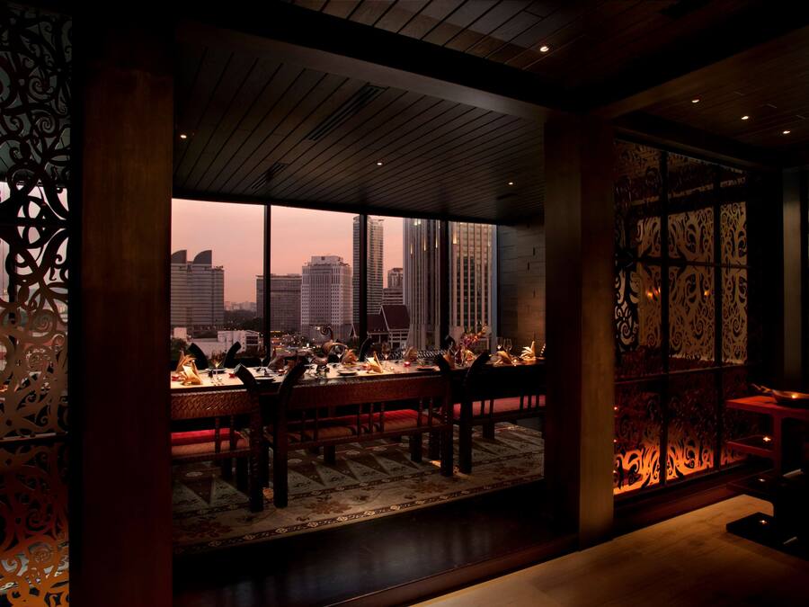 A dining area with a city view, featuring a wooden ceiling, patterned decor, and a table set for a meal.