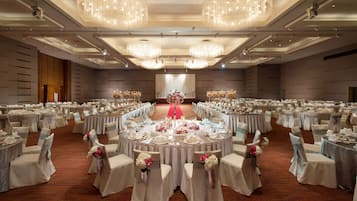Un gran salón de banquetes con mesas redondas, sillas y candelabros.