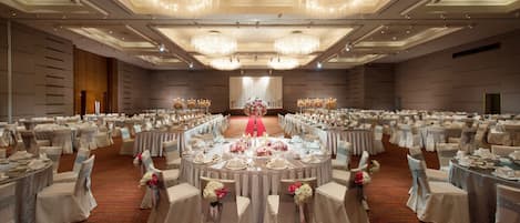 Un gran salón de banquetes con mesas redondas, sillas y candelabros.