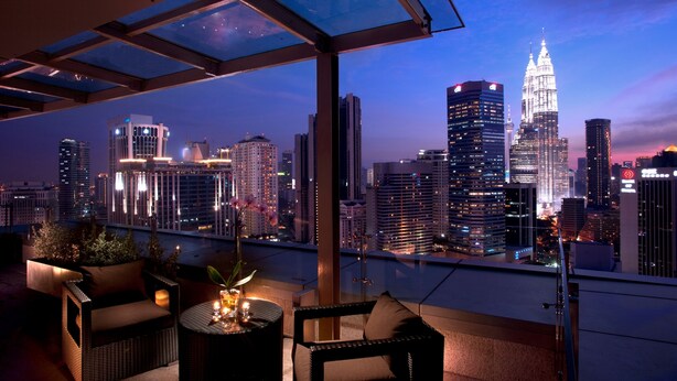 A rooftop terrace with a glass ceiling, offering a panoramic view of a city skyline at dusk.