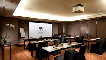 A hotel conference room with a large screen displaying "DOUBLETREE by Hilton Kuala Lumpur", multiple tables with chairs, and a carpeted floor.