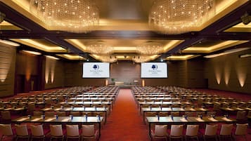 A conference room with rows of tables and chairs, large chandeliers, and two screens displaying the DoubleTree Kuala Lumpur logo.