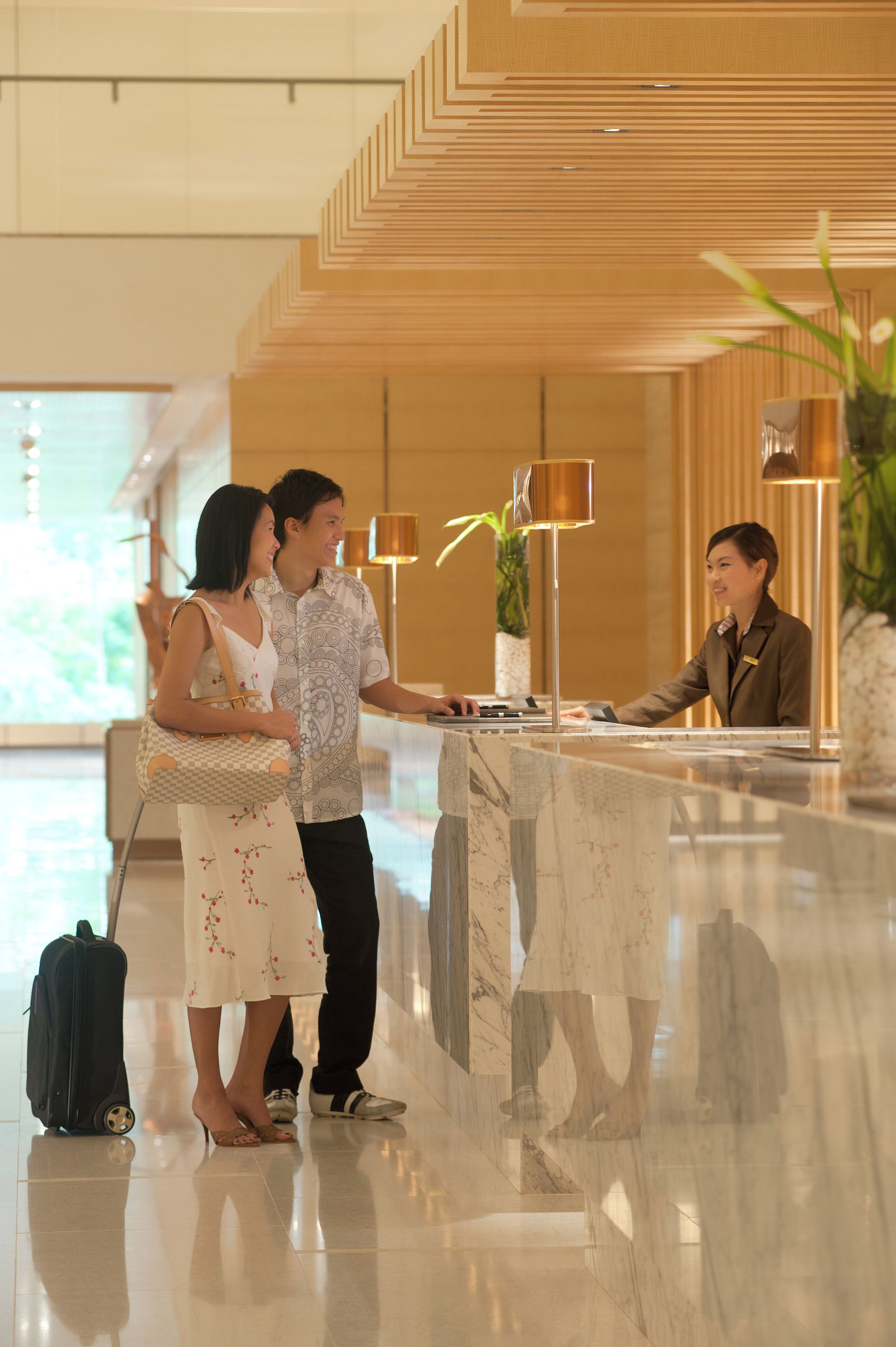 Een hotel receptie met een marmeren balie, een receptionist en een koppel dat daar staat.