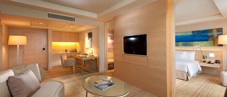 Una habitación de hotel moderna con sofá, una mesa de centro de vidrio, televisión, escritorio con silla y cama.