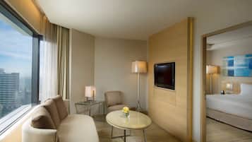 A hotel room with a bed, a sofa, a small table with a vase, a TV, and a window with curtains.