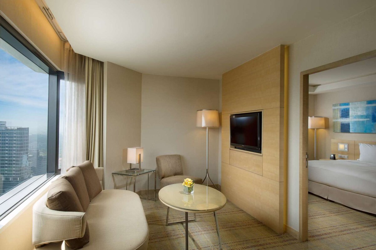 A hotel room with a sofa, a small table, a TV mounted on the wall, and a bed.