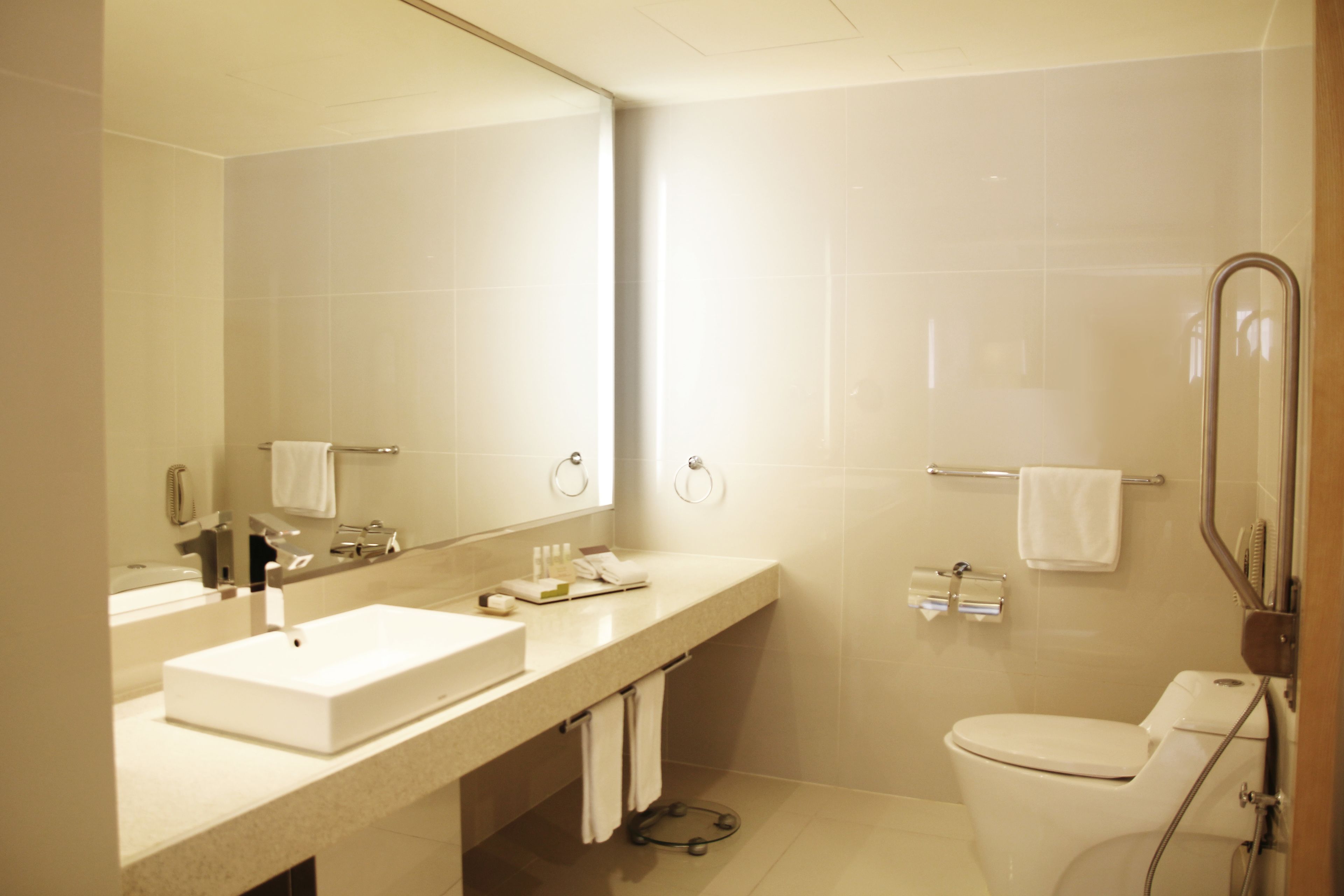 A modern bathroom with a large mirror, two sinks, a toilet, and a shower area.