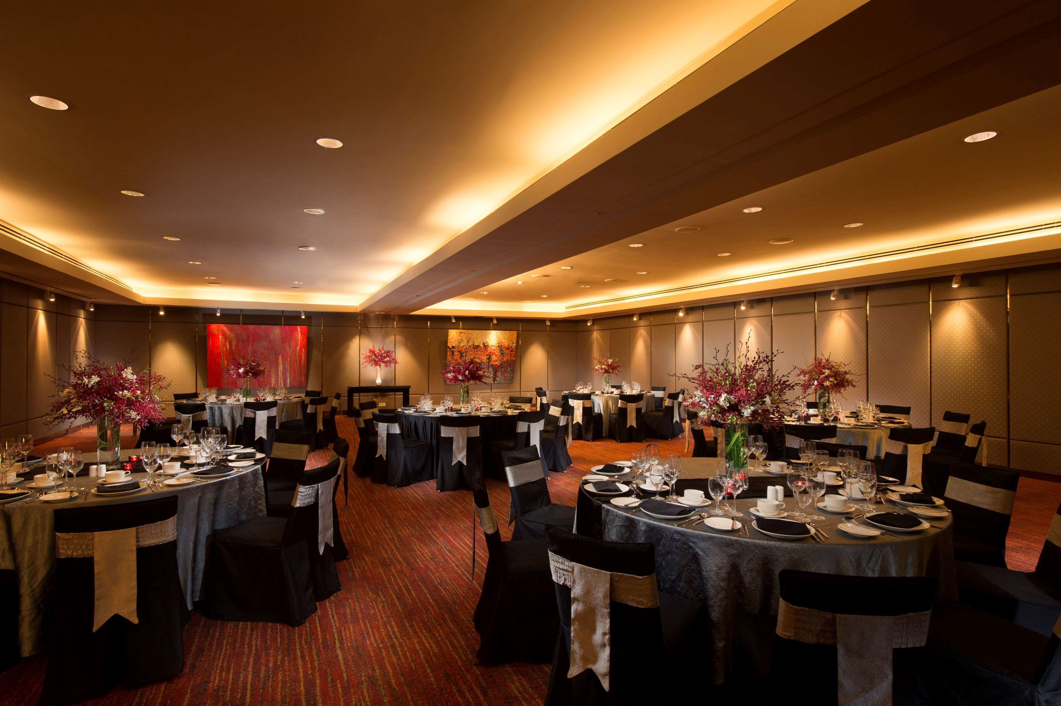 A banquet hall with round tables set for dining, black chairs, and floral centerpieces.