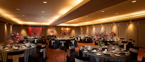 A banquet hall with round tables set for dining, black chairs, and floral centerpieces.