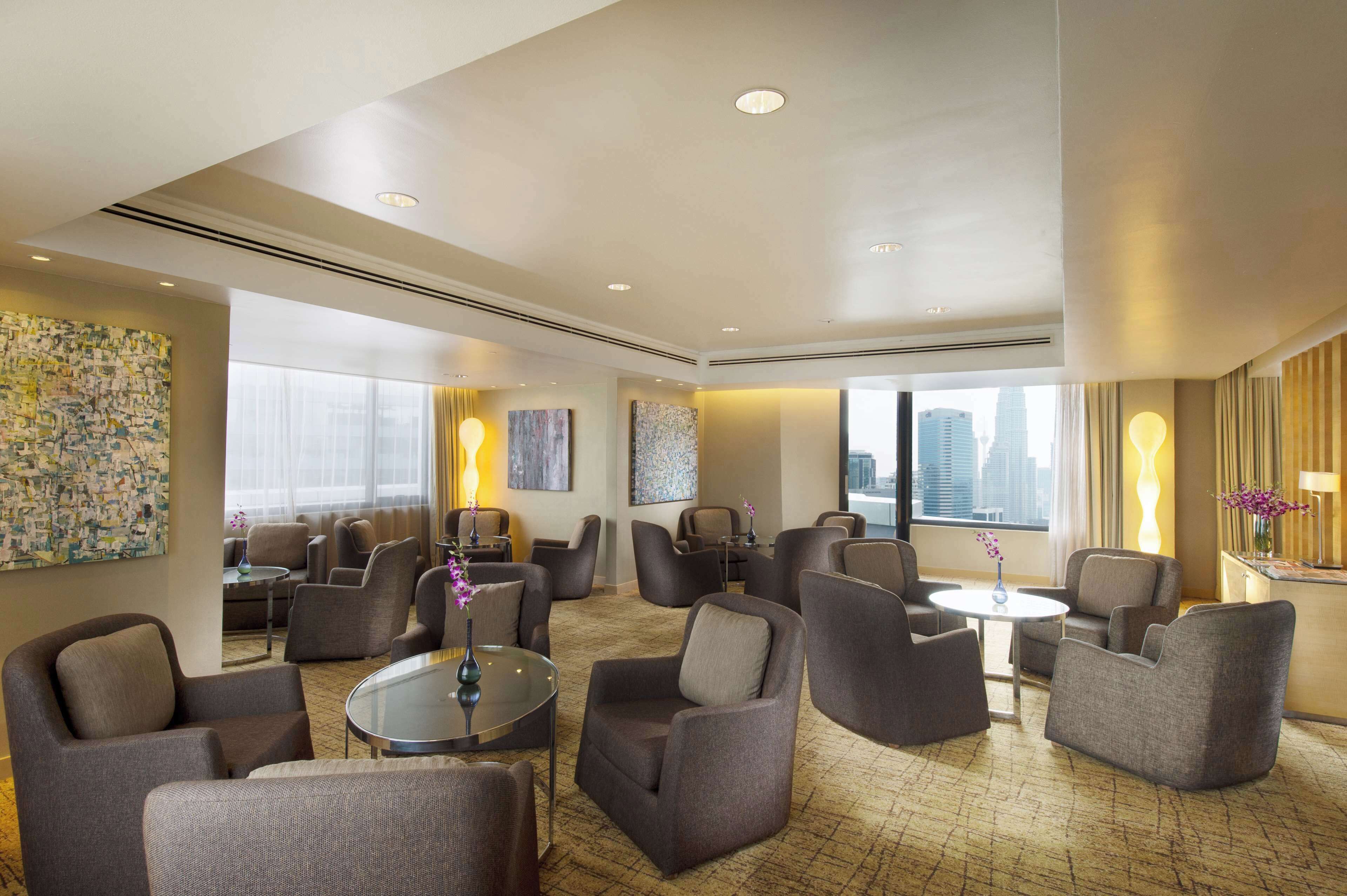 A spacious hotel lobby with multiple seating areas, large windows offering city views, and contemporary artwork on the walls.