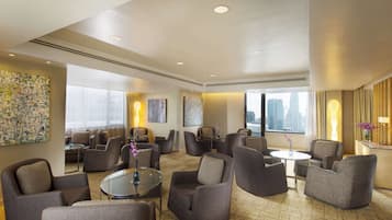 Een ruime hotel lobby met meerdere zithoeken, grote ramen met uitzicht op de stad en moderne kunst aan de muren.