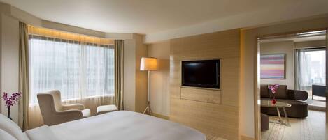 A hotel room with a large bed, a TV mounted on the wall, a sofa, and a small table with a vase of flowers.
