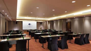 A conference room with multiple tables, chairs, and a projector screen displaying a presentation.