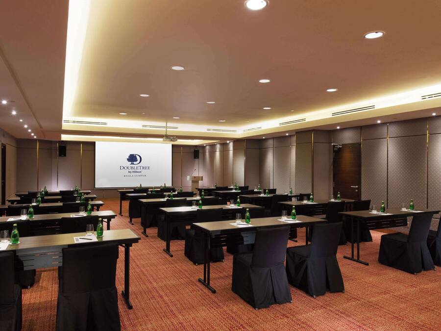 A conference room with multiple tables, chairs, and a projector screen displaying a presentation.