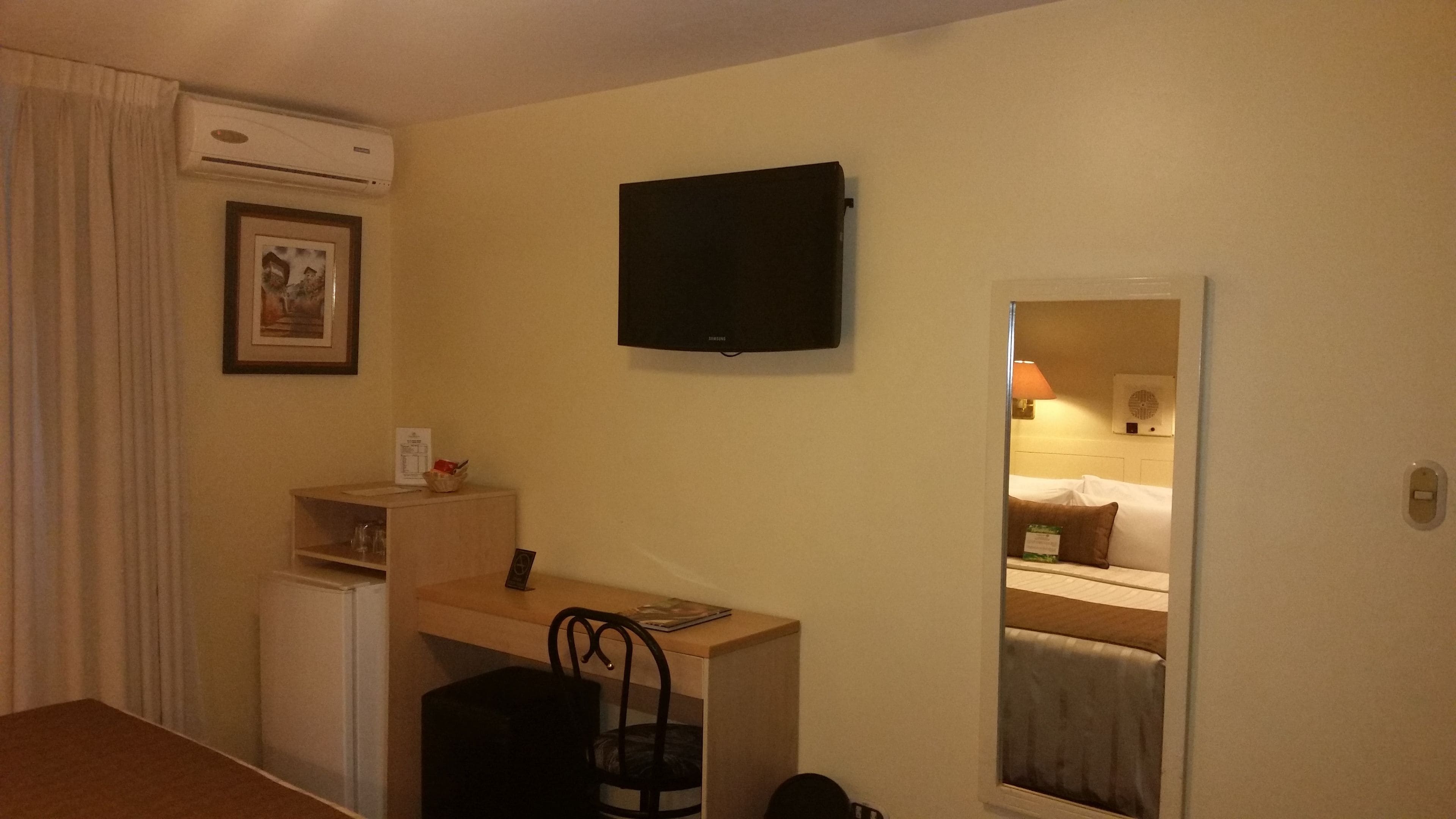 A hotel room with a desk, chair, and a television mounted on the wall.