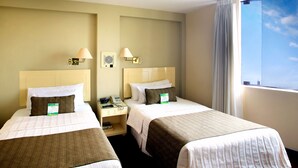 Une chambre d’hôtel avec deux lits, une table de chevet, une lampe, un téléphone et une fenêtre avec des rideaux.