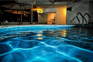 A swimming pool with clear water, a sunken bench, and a lounge area with umbrellas. - Embajadores Hotel (Lima)