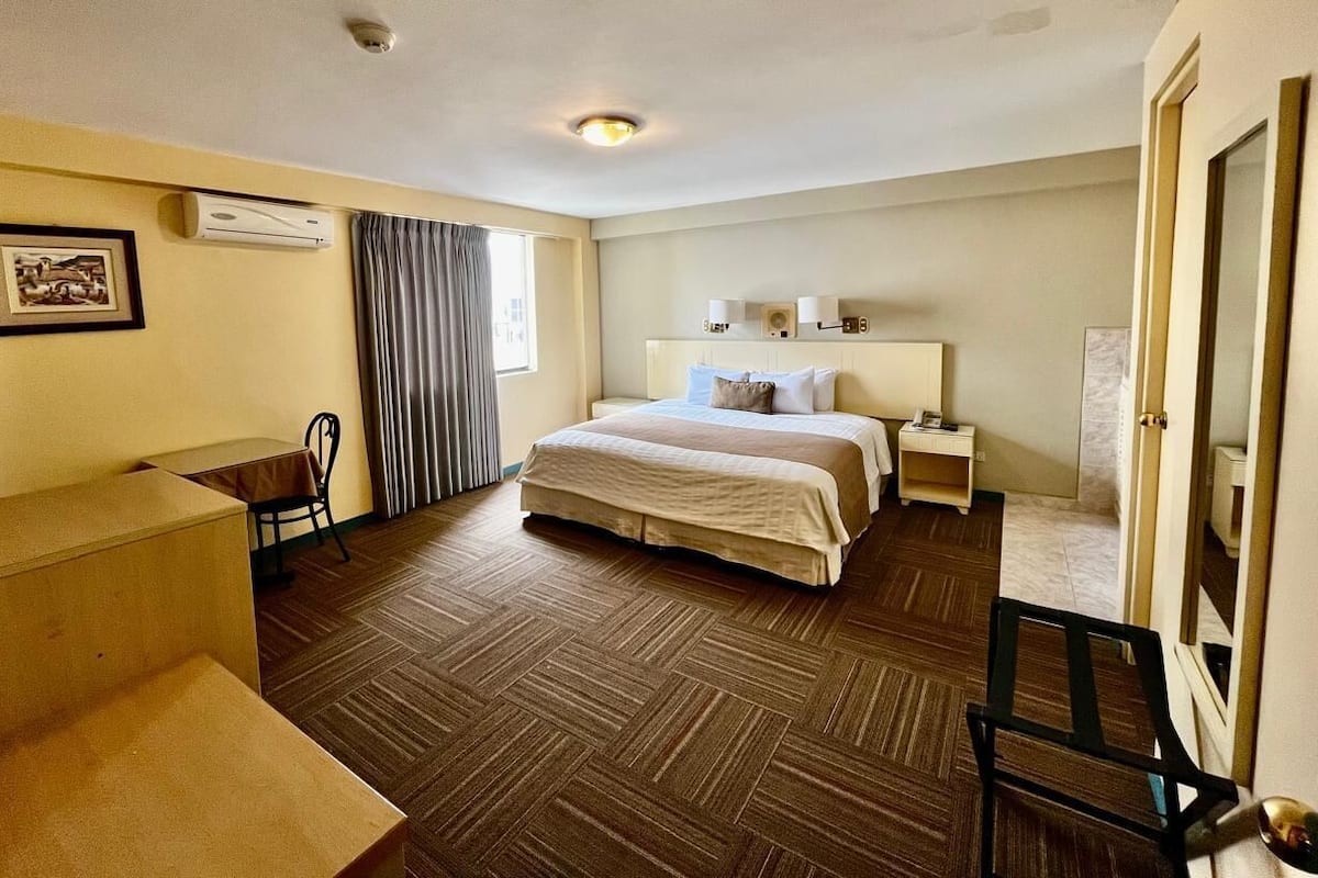 A hotel room with a large bed, a desk, a chair, a bedside table with lamps, and a picture on the wall.