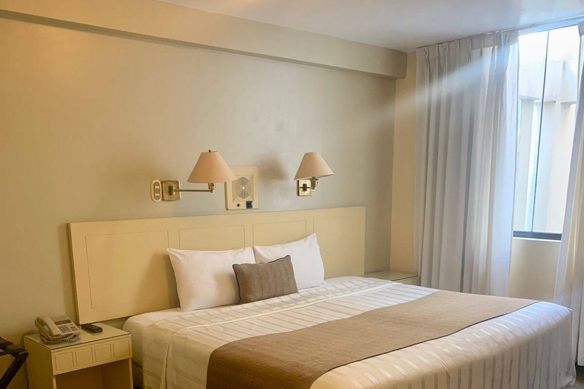 A hotel room with a large bed, two bedside lamps, a bedside phone, and a window with curtains.