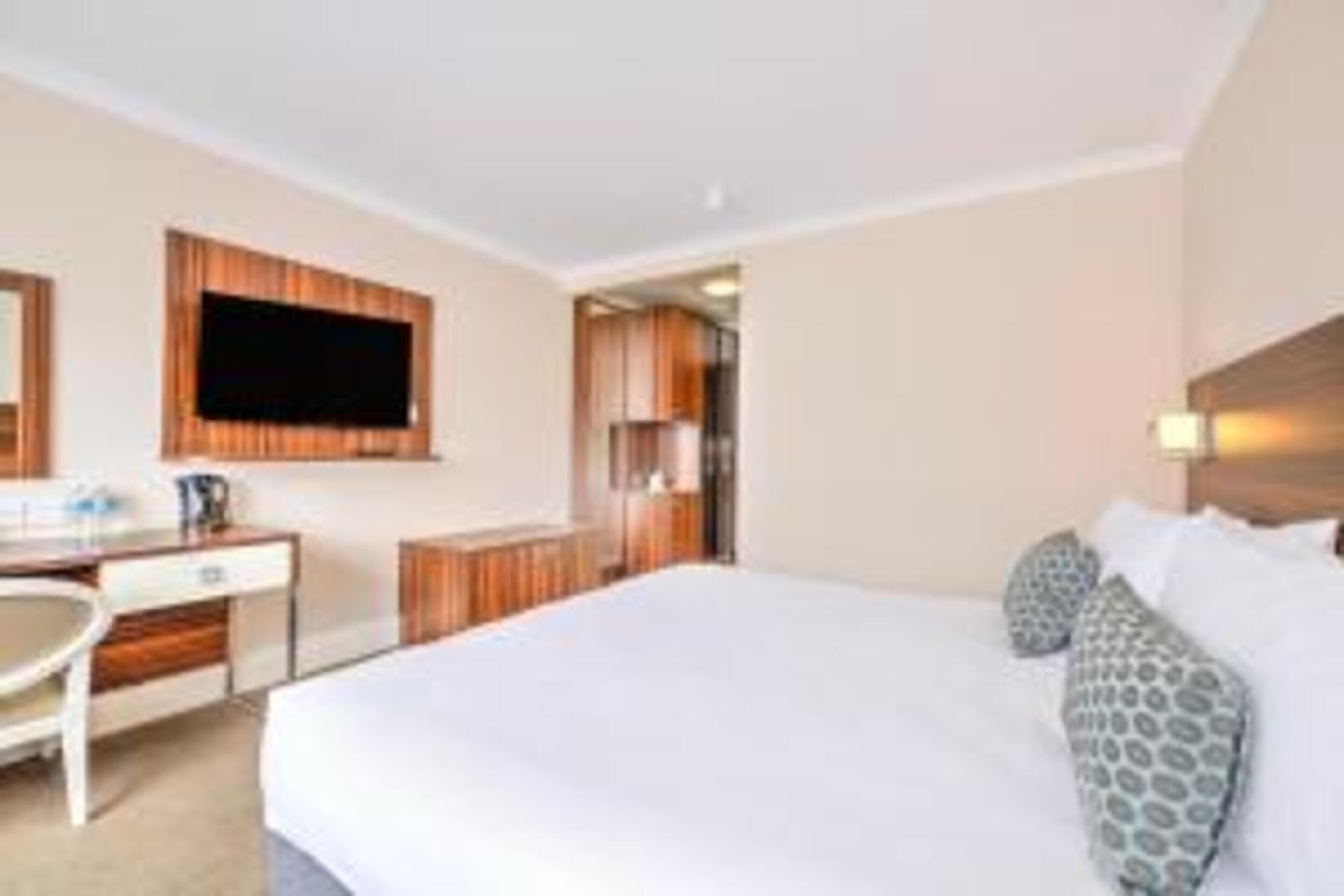A hotel room with a bed, a desk, a chair, a television, and a bathroom visible through an open door.