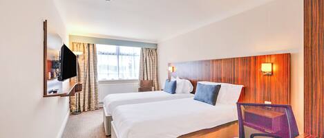 A hotel room with two beds, a desk, a chair, a TV, and a window with curtains.