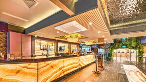 A hotel reception area with a marble counter, a chandelier, and a green wall with plants. - Palms Hotel & Retreat By Palette London Romford (Hornchurch)