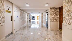 A hallway with marble flooring, ornate wallpaper, and doors labeled "Ladies." - Palms Hotel & Retreat By Palette London Romford (Hornchurch)
