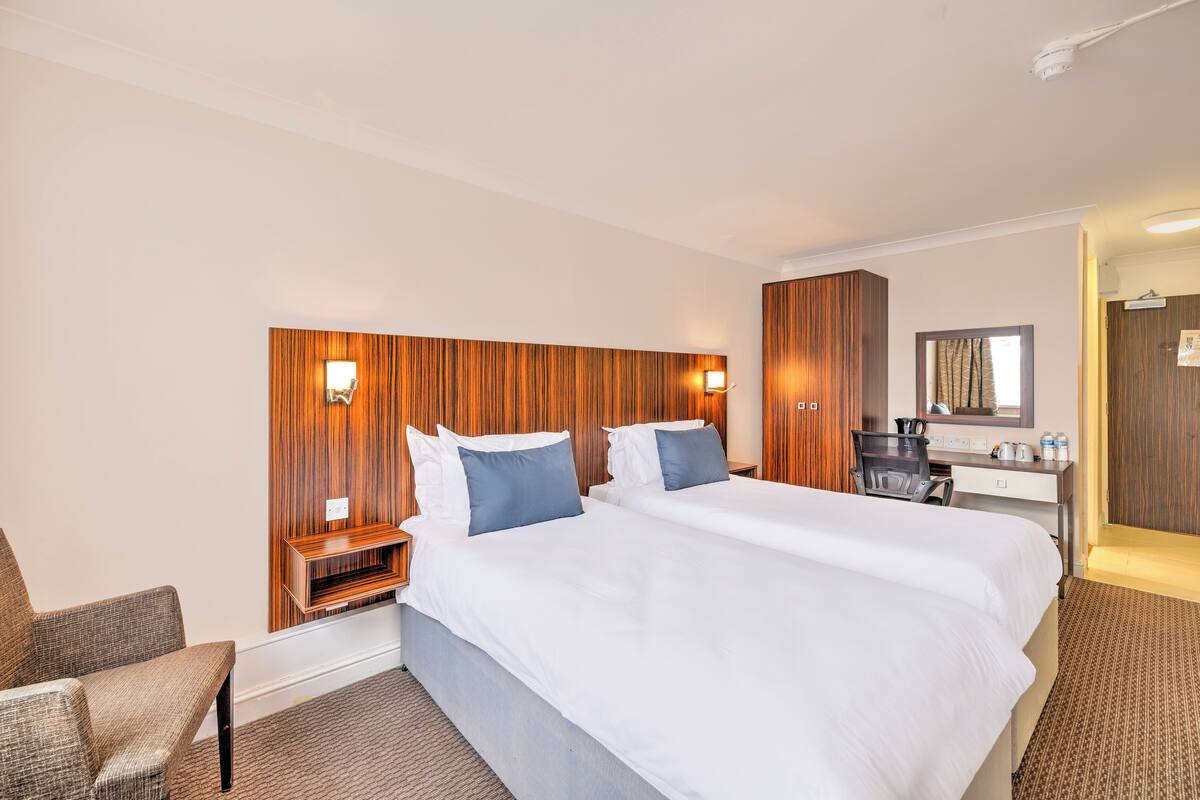 Una habitación de hotel con una cama grande, dos mesitas de noche, un escritorio con una silla, un armario y un espejo.