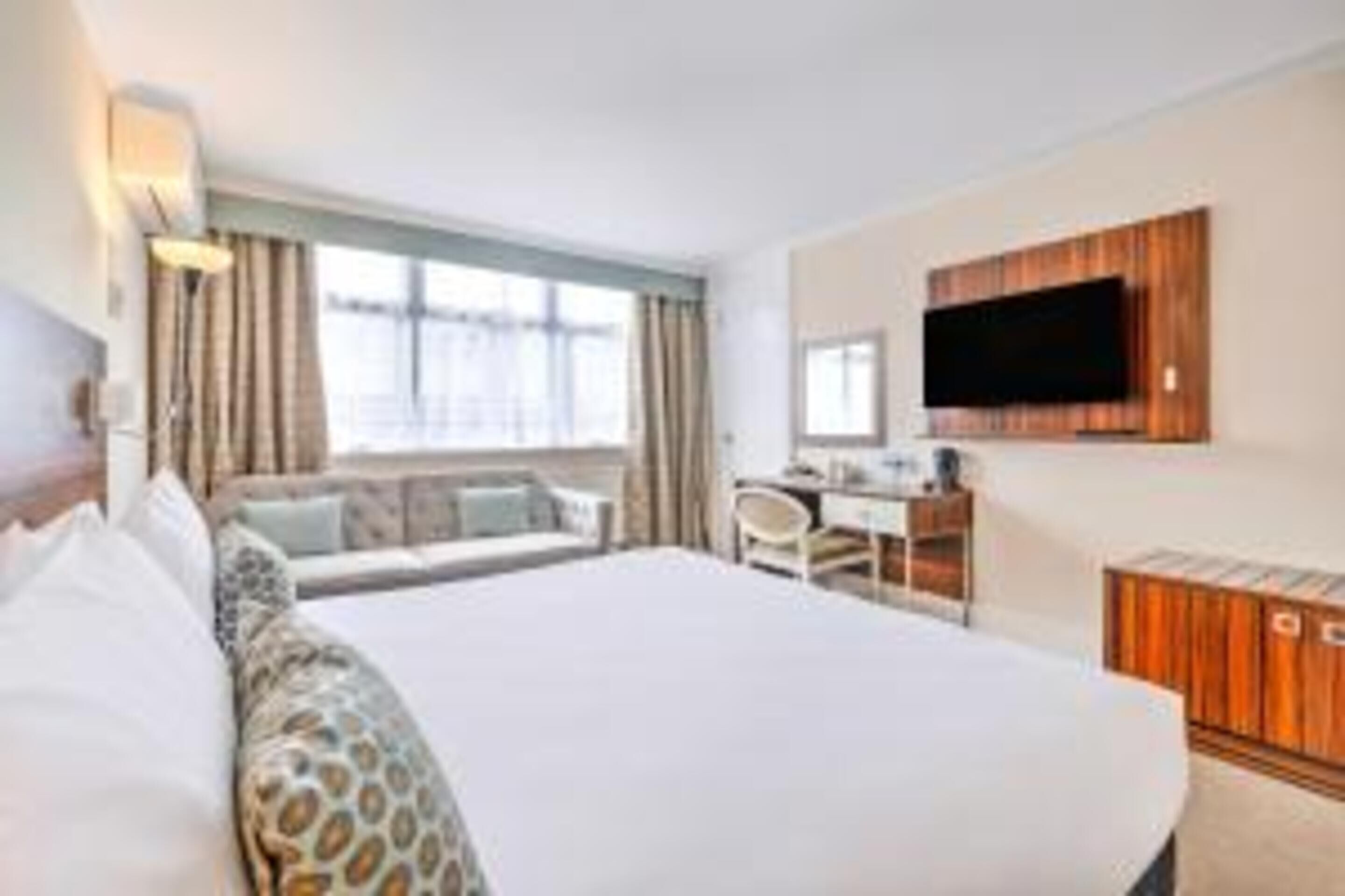 Een hotelkamer met een groot bed, een bureau, een flatscreen televisie aan de muur en een raam met gordijnen.