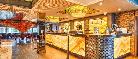 A modern hotel lobby with a marble reception desk, seating area, and decorative plants.