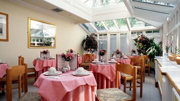 A dining area with tables covered in pink tablecloths, wooden chairs, and floral centerpieces.