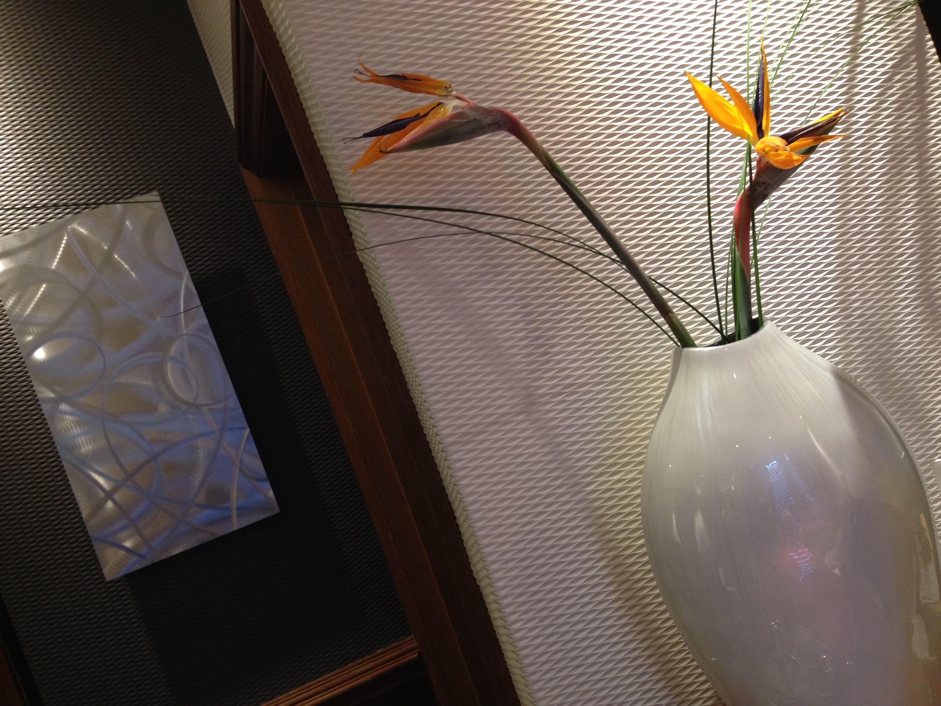 A vase with a plant on a textured wall.