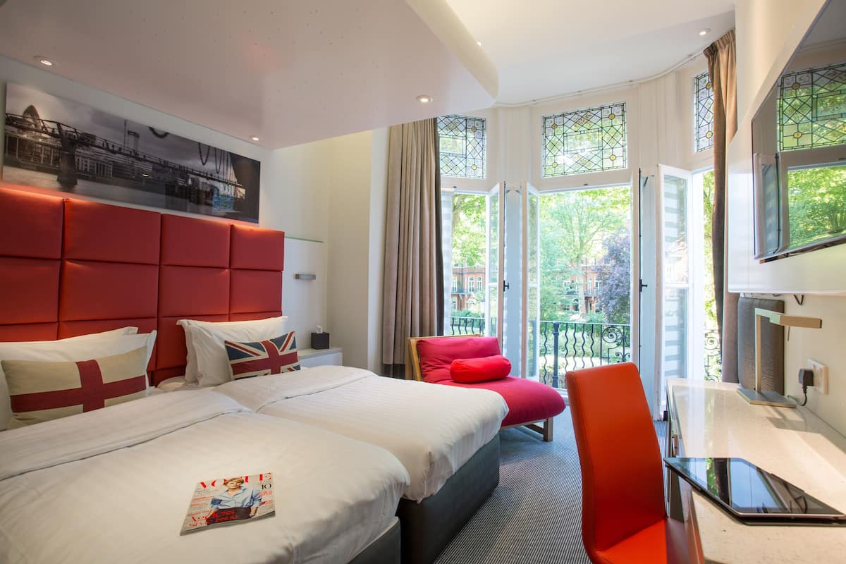 A hotel room with a large bed, a desk, a chair, and a balcony with a view.
