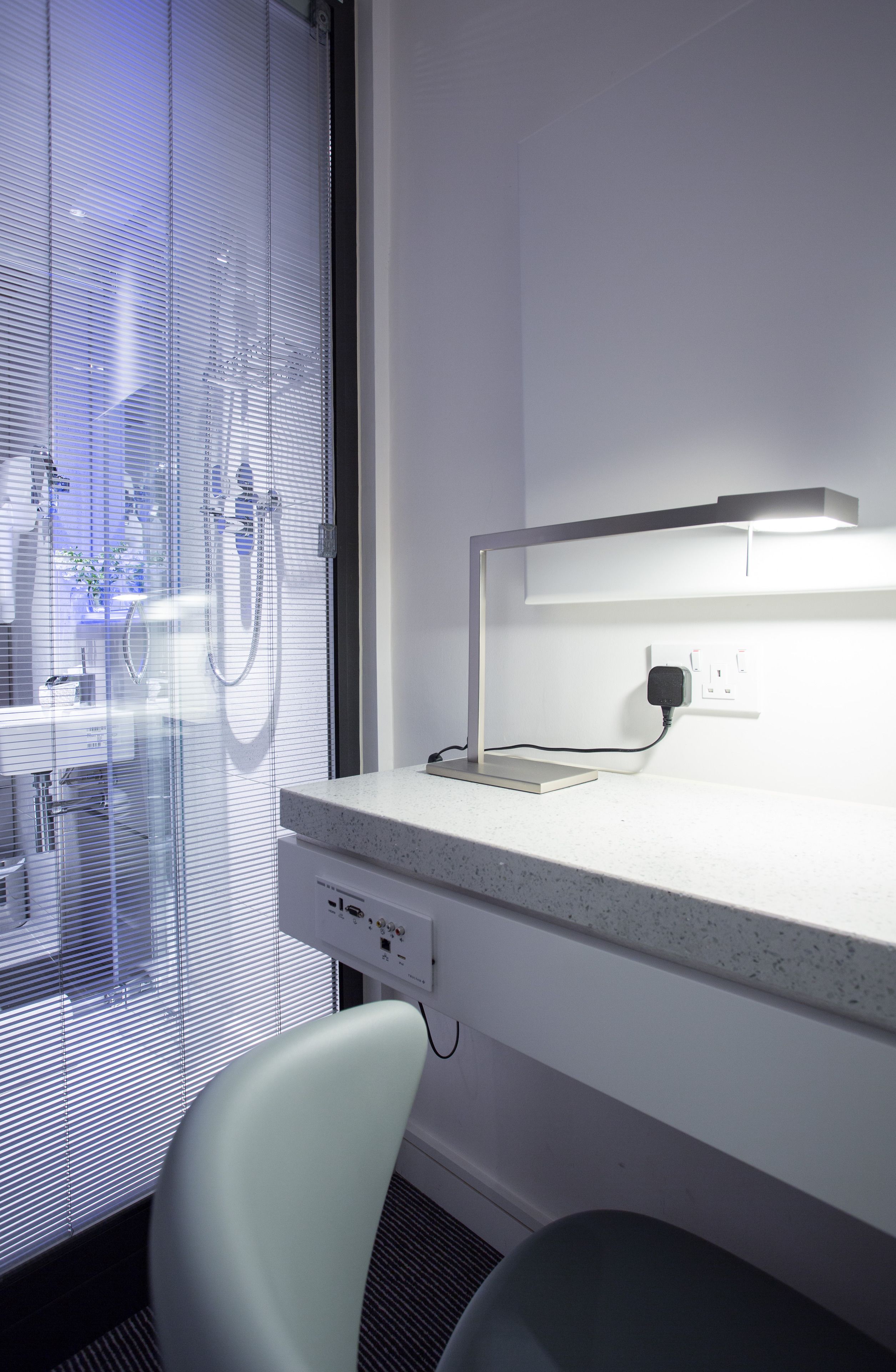 Un baño moderno con cabina de ducha de vidrio, encimera blanca y lámpara de escritorio.