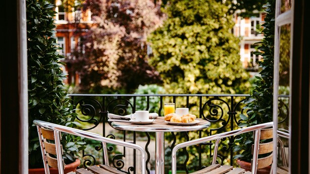 A balcony with two metal chairs and a small round table, a potted plant, and a breakfast setting with croissants, a cup, and a glass of orange juice. - Henley House Hotel (London)