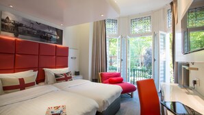 A hotel room with a large bed, a desk, a chair, and a balcony with a view of greenery. - Henley House Hotel (London)