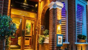 The entrance of Henley House Hotel with a checkered tile floor, brick walls, and a wooden door. - Henley House Hotel (London)