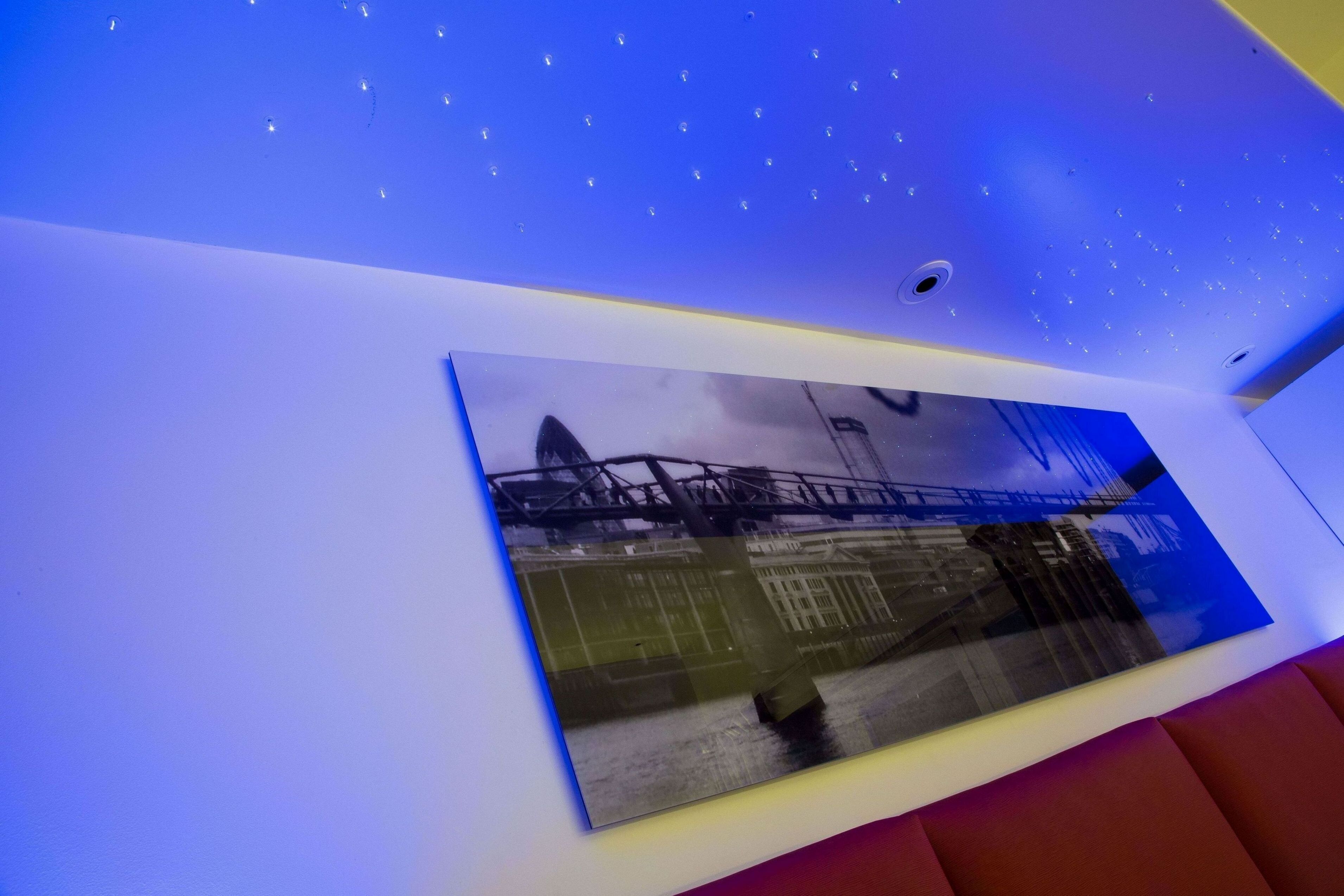 A room with a large framed photograph on the wall, a ceiling with small lights, and a red cushioned seating area.