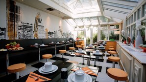A modern cafe with a black and white checkered floor, orange stools, and a glass ceiling allowing natural light. - Henley House Hotel (London)