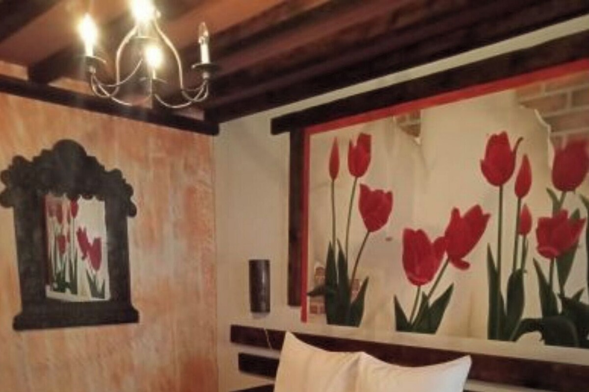 Habitación de hotel con una cama grande, una araña y un cuadro de tulipanes rojos en la pared.